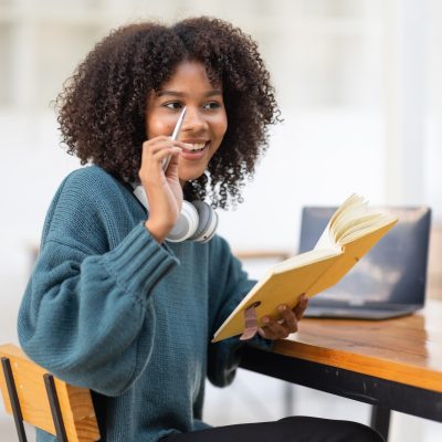 Cute african american female student wearing headphones with afro dreadlocks, studying remotely from