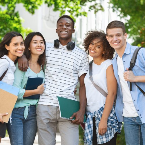 Group of international students posing in front of university, looking at camera and smiling
